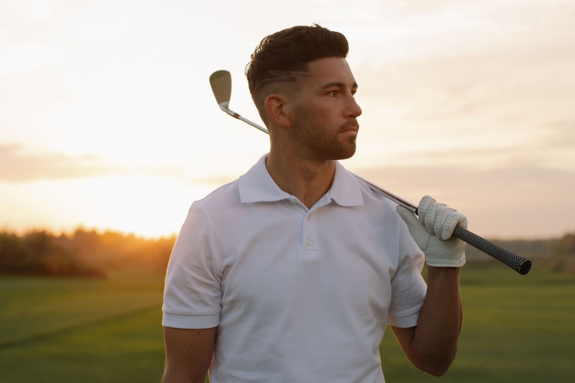 A golfer in a plain white polo at sunset, club over the shoulder